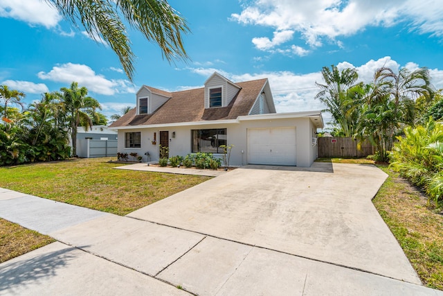 new england style home featuring a garage, concrete driveway, fence, a front yard, and stucco siding