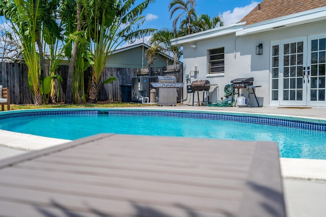 view of swimming pool featuring french doors, area for grilling, fence, and a fenced in pool