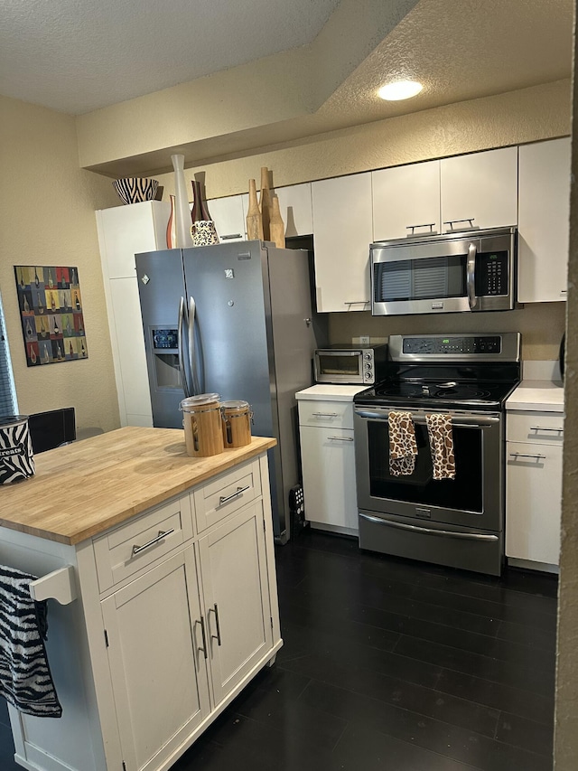 kitchen featuring butcher block countertops, white cabinetry, a textured ceiling, and appliances with stainless steel finishes