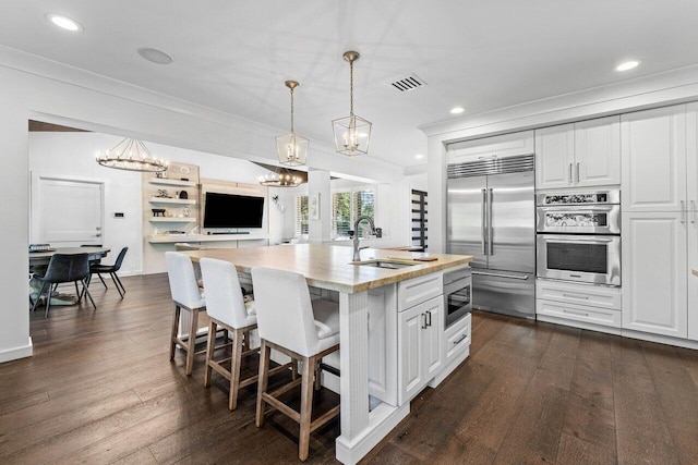 kitchen featuring sink, built in appliances, decorative light fixtures, a center island with sink, and white cabinets