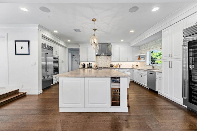 kitchen featuring stainless steel appliances, wall chimney range hood, tasteful backsplash, decorative light fixtures, and a kitchen island with sink