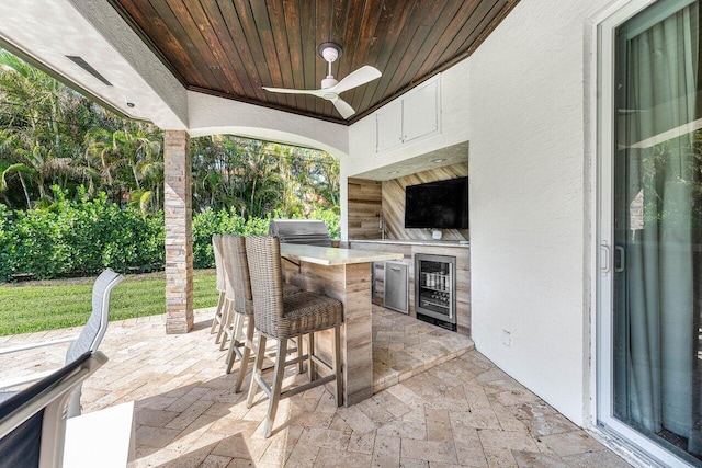 view of patio featuring exterior bar, area for grilling, ceiling fan, and beverage cooler