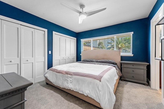 bedroom with ceiling fan, light colored carpet, and multiple closets