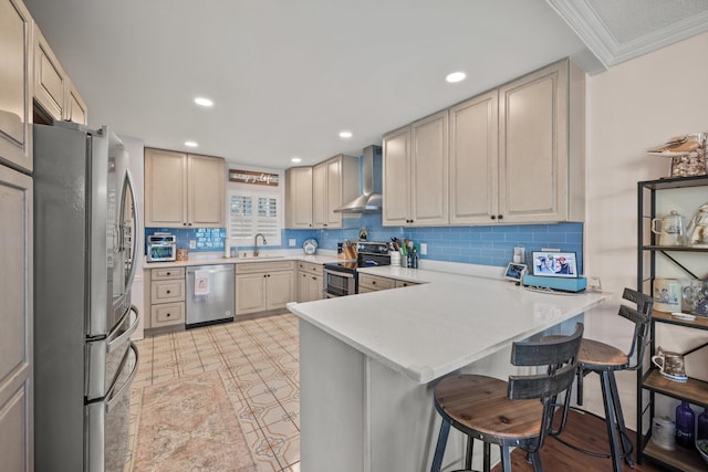 kitchen featuring wall chimney exhaust hood, stainless steel appliances, kitchen peninsula, a kitchen bar, and ornamental molding