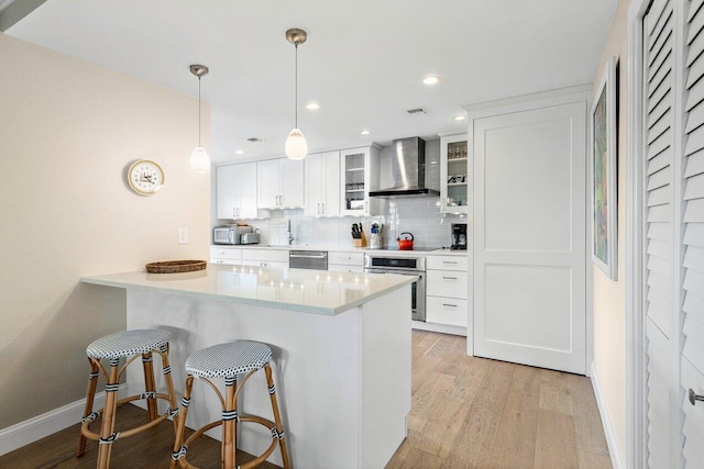 kitchen featuring wall chimney exhaust hood, appliances with stainless steel finishes, white cabinets, pendant lighting, and backsplash