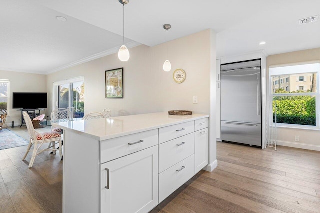 kitchen with pendant lighting, crown molding, built in refrigerator, light hardwood / wood-style floors, and white cabinets