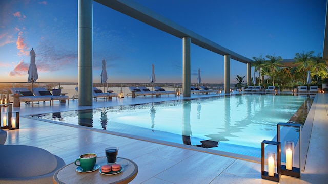 pool at dusk featuring a patio area and a water view