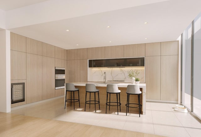 kitchen featuring light tile patterned flooring, a kitchen island with sink, light brown cabinetry, and a breakfast bar area