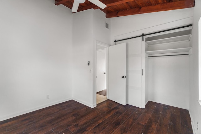 unfurnished bedroom with ceiling fan, dark wood-type flooring, a barn door, lofted ceiling with beams, and a closet