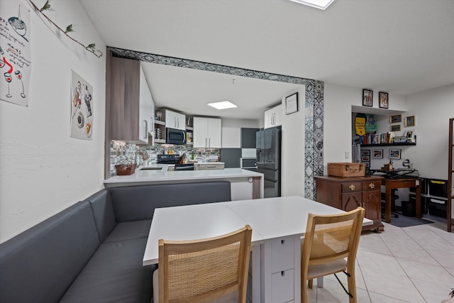 kitchen with white cabinets, a kitchen breakfast bar, black appliances, light tile patterned floors, and kitchen peninsula