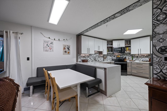 kitchen with white cabinets, kitchen peninsula, black electric range oven, and light tile patterned floors