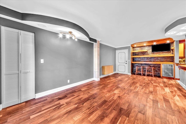 unfurnished living room featuring built in features, light hardwood / wood-style flooring, beverage cooler, and ornamental molding