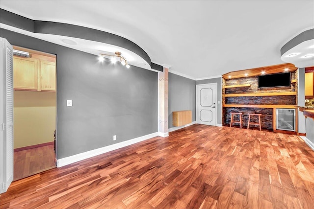 unfurnished living room with light hardwood / wood-style floors, built in features, beverage cooler, and crown molding