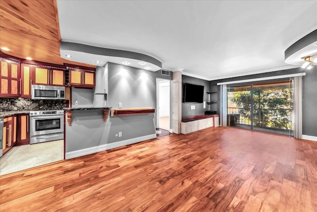 kitchen with dark stone counters, ornamental molding, light wood-type flooring, appliances with stainless steel finishes, and tasteful backsplash