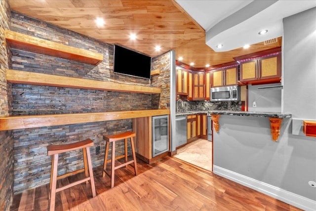 kitchen featuring a kitchen breakfast bar, kitchen peninsula, dark stone countertops, decorative backsplash, and appliances with stainless steel finishes