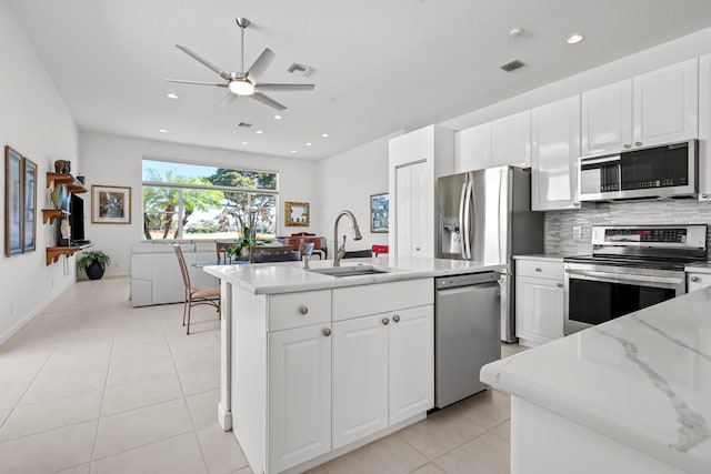 kitchen with light stone counters, stainless steel appliances, sink, light tile patterned floors, and white cabinets