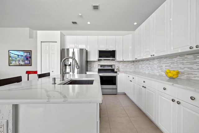 kitchen with white cabinets, appliances with stainless steel finishes, a kitchen island with sink, and sink