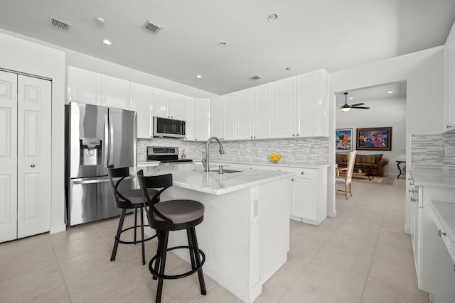 kitchen featuring light stone countertops, appliances with stainless steel finishes, ceiling fan, sink, and an island with sink