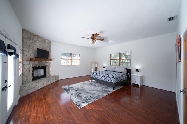 bedroom with a stone fireplace, ceiling fan, and dark wood-type flooring