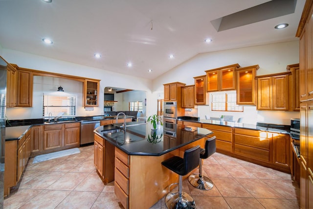 kitchen with a kitchen breakfast bar, stainless steel appliances, vaulted ceiling, a kitchen island with sink, and light tile patterned flooring