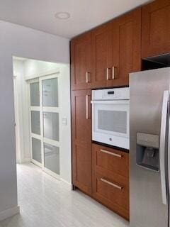 kitchen with brown cabinetry, oven, stainless steel refrigerator with ice dispenser, and baseboards