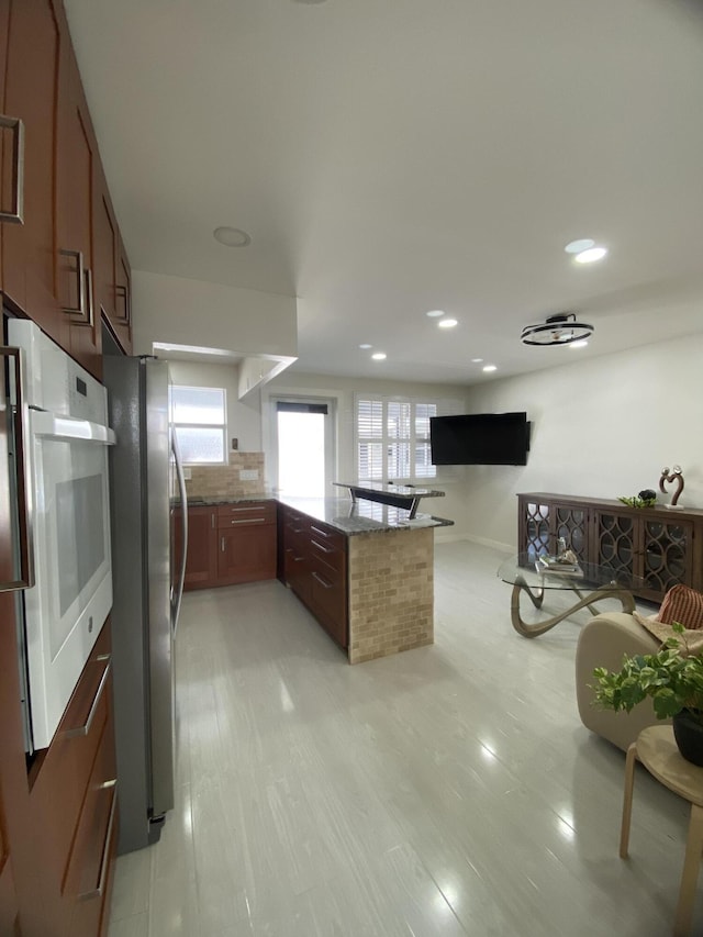 kitchen with oven, a peninsula, backsplash, freestanding refrigerator, and dark stone counters