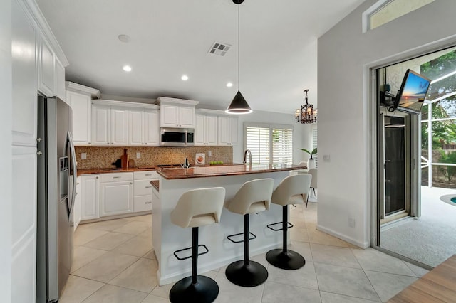 kitchen with butcher block counters, hanging light fixtures, an island with sink, stainless steel appliances, and white cabinets