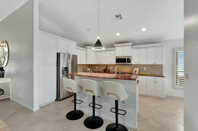 kitchen with lofted ceiling, appliances with stainless steel finishes, butcher block counters, white cabinets, and a center island with sink