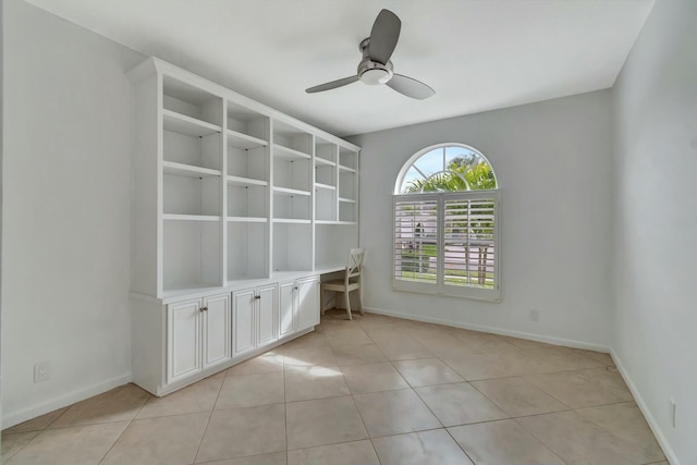 tiled empty room featuring built in desk and ceiling fan