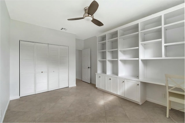 unfurnished bedroom with built in desk, ceiling fan, and a closet