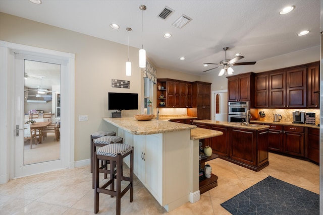 kitchen featuring kitchen peninsula, decorative backsplash, double oven, hanging light fixtures, and a breakfast bar area