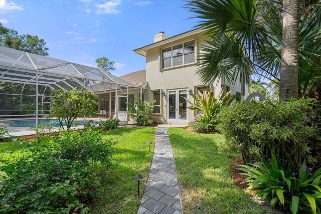 rear view of property with a lawn, glass enclosure, and french doors