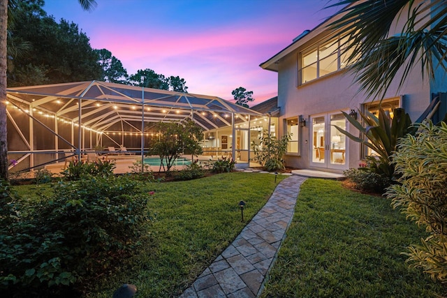 yard at dusk featuring glass enclosure and french doors