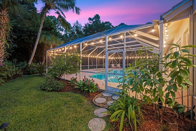 pool at dusk with a yard and glass enclosure