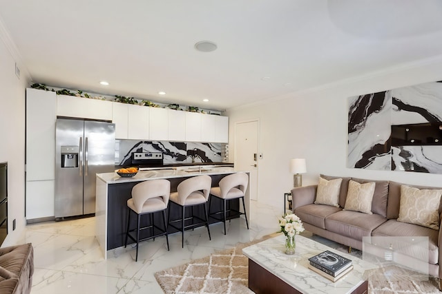 kitchen featuring backsplash, white cabinets, stainless steel fridge, ornamental molding, and a kitchen bar