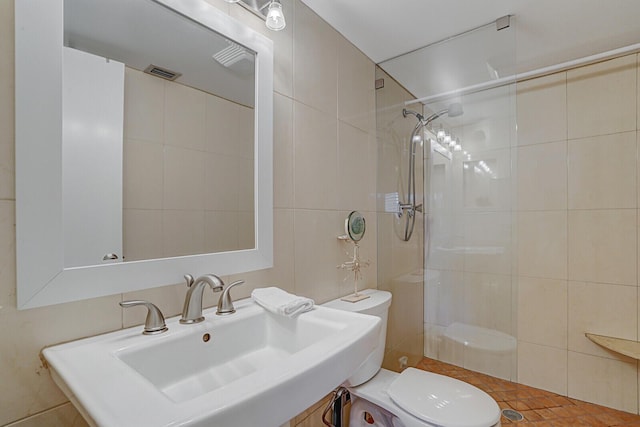 bathroom with a tile shower, sink, tile walls, and toilet