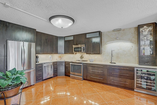 kitchen featuring beverage cooler, a textured ceiling, dark brown cabinets, light tile patterned floors, and appliances with stainless steel finishes