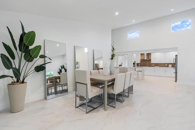 dining room with recessed lighting, marble finish floor, a towering ceiling, and baseboards