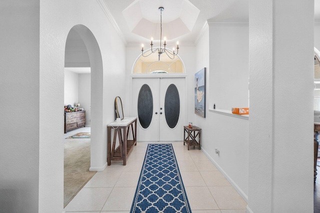 tiled foyer with a raised ceiling, ornamental molding, french doors, and a chandelier