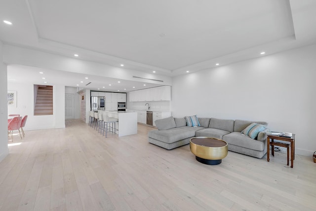 living room with a tray ceiling, sink, and light hardwood / wood-style floors