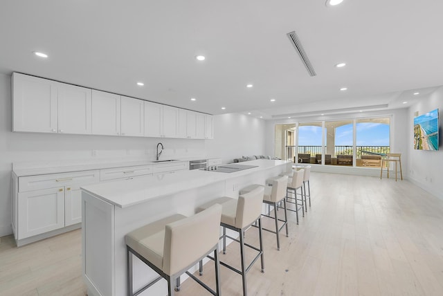 kitchen featuring a breakfast bar, sink, light hardwood / wood-style flooring, a center island, and white cabinetry