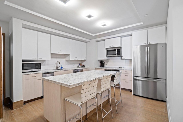 kitchen with a kitchen bar, stainless steel appliances, sink, white cabinetry, and a kitchen island