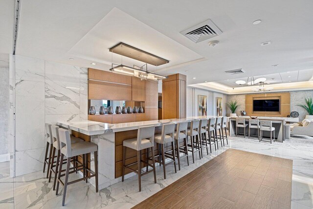 kitchen featuring a raised ceiling, kitchen peninsula, a breakfast bar area, and hanging light fixtures