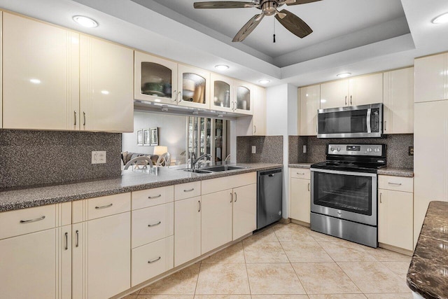 kitchen featuring decorative backsplash, stainless steel appliances, a raised ceiling, ceiling fan, and cream cabinetry