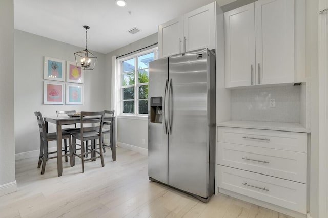 kitchen featuring pendant lighting, light hardwood / wood-style flooring, stainless steel fridge, white cabinetry, and a chandelier