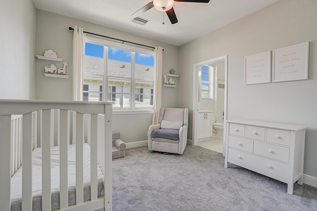 bedroom featuring ceiling fan, a crib, light carpet, and ensuite bath