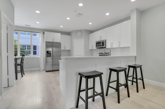 kitchen featuring kitchen peninsula, appliances with stainless steel finishes, tasteful backsplash, white cabinetry, and a breakfast bar area