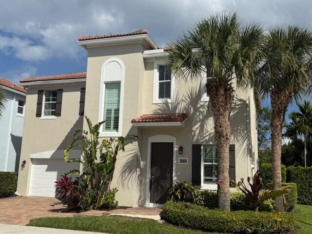 mediterranean / spanish home with a garage, decorative driveway, a tiled roof, and stucco siding