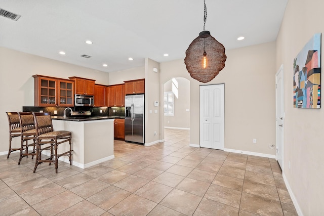 kitchen with arched walkways, visible vents, appliances with stainless steel finishes, dark countertops, and glass insert cabinets