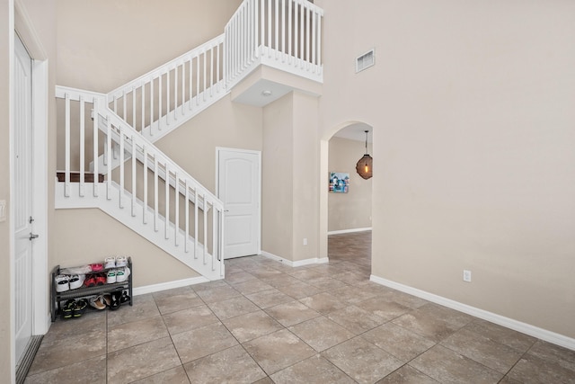 tiled foyer with baseboards, a high ceiling, arched walkways, and stairs